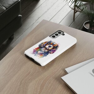 May include: A white phone case featuring a watercolour painting of a Cavalier King Charles Spaniel dog. The dog is brown, black and white with splashes of colour.