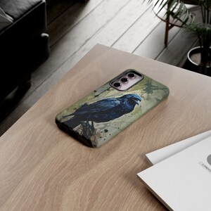 May include: A black phone case with a watercolor-style design of a raven perched on a branch. The case has a cutout for the camera lens and a textured surface.
