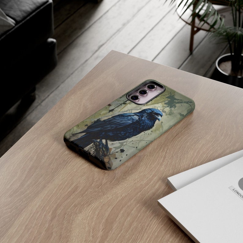 May include: A black phone case with a watercolor-style design of a raven perched on a branch. The case has a cutout for the camera lens and a textured surface.