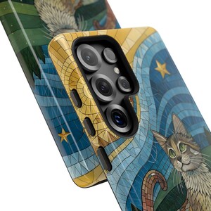 K&ouml;nnte beinhalten: Nahaufnahme von zwei Handyh&uuml;llen mit Mosaikdesign. Eine H&uuml;lle zeigt eine Katzenillustration mit blauem und goldenem Hintergrund. Die andere H&uuml;lle hat ein &auml;hnliches Design mit einer Vogelillustration. Die H&uuml;llen haben ein schwarzes Kameramodul.