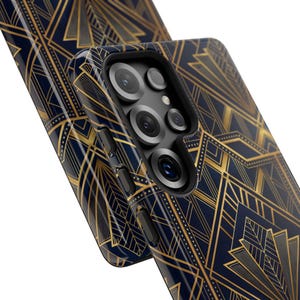 May include: Two navy blue phone cases with a gold Art Deco pattern. The phone case on the right has a camera bump with multiple lenses and buttons on the side. The design is a repeating geometric pattern.