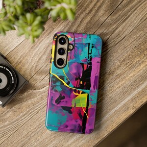 Op de afbeelding: Een telefoonhoesje met een abstract ontwerp in levendige kleuren zoals turquoise, paars, roze, geel en zwart. De hoes heeft een uitsparing voor een drievoudige camera lens.