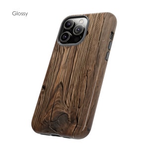 Op de afbeelding: Een glanzende telefoonhoes van houtnerf voor een iPhone met een camerabult. De hoes is bruin met een donker houtnerfpatroon.