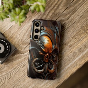 May include: A black phone case with a detailed, metallic, skull design. The skull is orange and blue with a black background. The case has a triple camera lens.