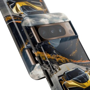 Puede incluir: Una funda para tel&eacute;fono con un coche deportivo amarillo conduciendo por una carretera de monta&ntilde;a sinuosa. La funda tiene una protuberancia de c&aacute;mara negra y dorada con tres lentes.