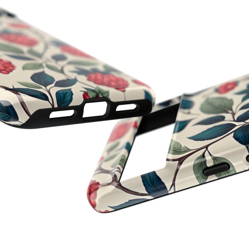 K&ouml;nnte beinhalten: Nahaufnahme von zwei Handyh&uuml;llen. Sie zeigen ein cremefarbenes Blumenmuster mit roten Beeren, gr&uuml;nen Bl&auml;ttern und dunkelbraunen Stielen. Die R&auml;nder der H&uuml;llen sind schwarz.