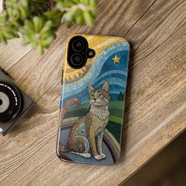 K&ouml;nnte beinhalten: Smartphone-H&uuml;lle mit einer Mosaik-Illustration einer Katze mit gr&uuml;nen Augen, vor dem Hintergrund eines Sternenhimmels, einer Sonne und eines Regenbogens. Auf einer Holzoberfl&auml;che.