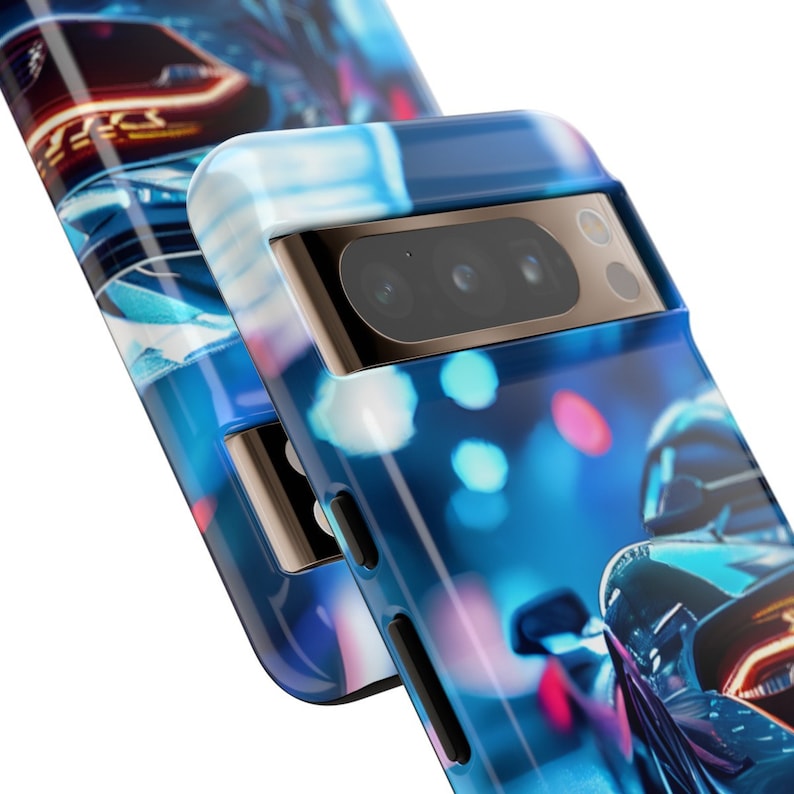 May include: A blue and black phone case featuring a blurred image of a car driving through a city at night. The case has a raised camera bump with three lenses.