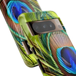 K&ouml;nnte beinhalten: Eine gr&uuml;ne, schwarze und blaue Handyh&uuml;lle mit einem Pfauenfeder-Design. Die H&uuml;lle hat eine erh&ouml;hte Kameraabdeckung mit drei Objektiven.