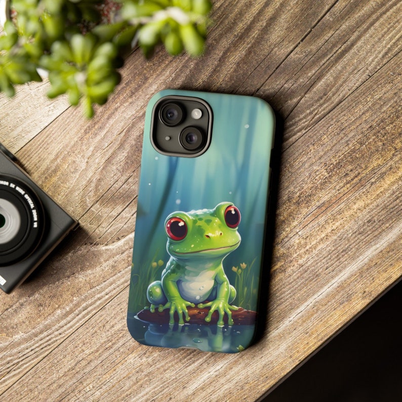May include: A green frog with red eyes sits on a branch in a pond. The frog is looking at the camera. The phone case is blue and green.