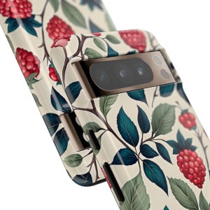 K&ouml;nnte beinhalten: Eine Handyh&uuml;lle mit cremefarbenem Hintergrund und einem sich wiederholenden Muster aus roten Himbeeren, gr&uuml;nen Bl&auml;ttern und braunen Stielen. Die H&uuml;lle hat einen Kameraausschnitt und einen Metallrahmen.