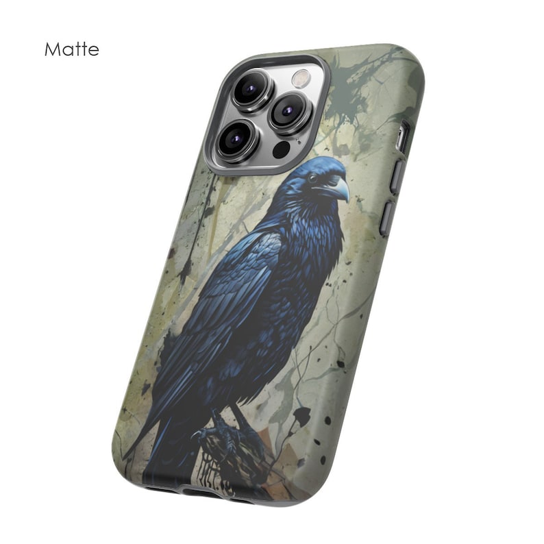 May include: A phone case with a matte finish featuring a black raven with a watercolor background. The case has a cutout for the camera lens and a textured design.