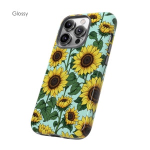 May include: A glossy phone case with a light blue background and a pattern of yellow sunflowers. The case is designed for an iPhone with a camera bump.