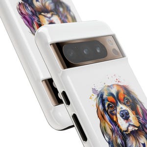 May include: White phone case featuring a watercolour painting of a Cavalier King Charles Spaniel dog. The case has a gold camera bump with three black lenses.