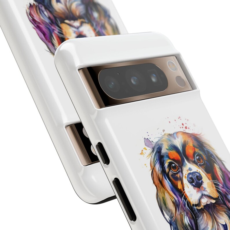 May include: White phone case featuring a watercolour painting of a Cavalier King Charles Spaniel dog. The case has a gold camera bump with three black lenses.