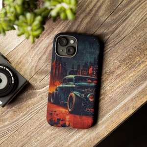 May include: A phone case with a vintage car illustration. The car is blue and has a red, orange, and yellow background. The case has a black background with a cityscape in the background.