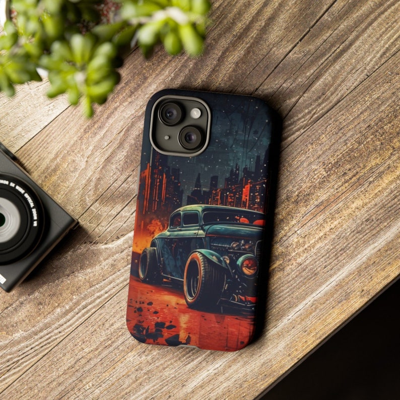 May include: A phone case with a vintage car illustration. The car is blue and has a red, orange, and yellow background. The case has a black background with a cityscape in the background.
