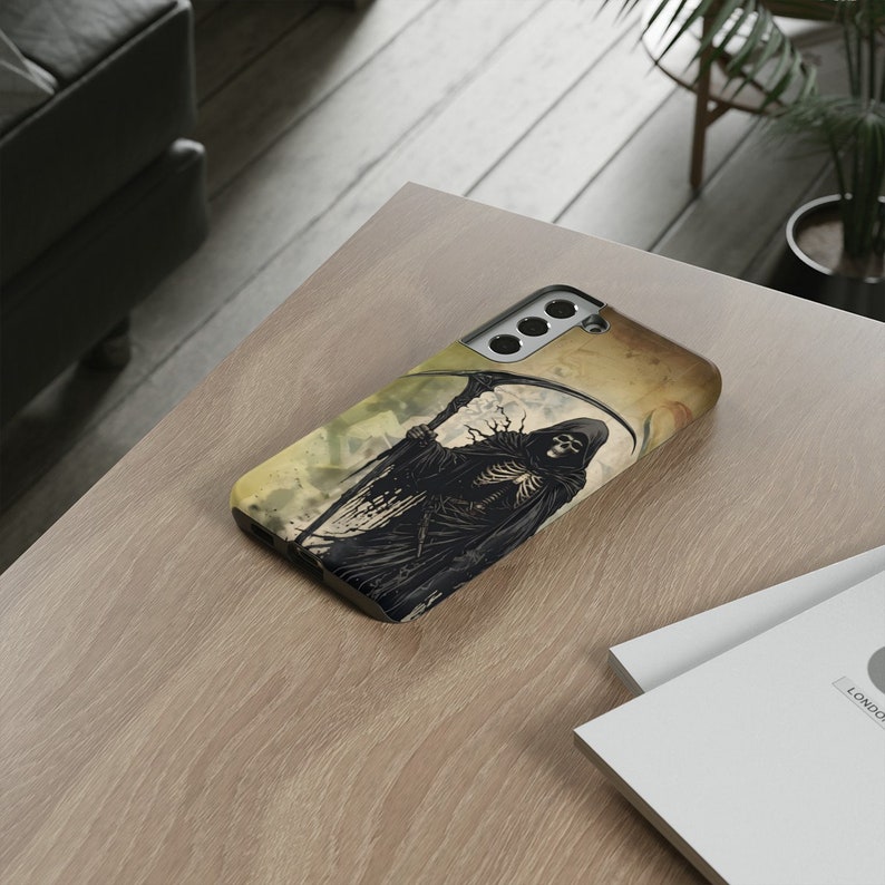 May include: A black phone case with a graphic of the Grim Reaper holding a scythe. The background is a faded yellow and brown watercolor design.