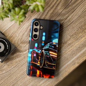 Puede incluir: Una funda de tel&eacute;fono negra con una imagen colorida de un coche deportivo conduciendo por una ciudad de noche. La funda tiene un recorte para la c&aacute;mara con tres lentes.