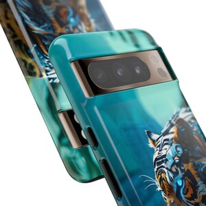 Puede incluir: Una funda para tel&eacute;fono de color azul turquesa con un gr&aacute;fico de un tigre con un ojo rob&oacute;tico. La funda tiene una protuberancia de c&aacute;mara elevada con tres lentes de c&aacute;mara negras.