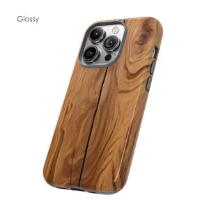 Może przedstawiać: Etui na telefon z błyszczącym wzorem drewna, ze srebrnym wystającym aparatem i trzema obiektywami. Etui jest przeznaczone do iPhone'a.