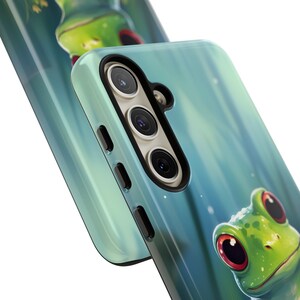 May include: A teal blue phone case with a green frog illustration. The case has a triple camera lens on the back.