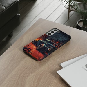 May include: A black phone case with a vintage car graphic. The car is green and has a red and orange background. The case has a cityscape in the background.