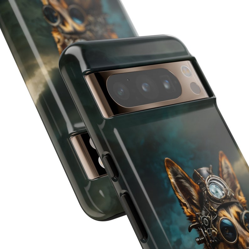 K&ouml;nnte beinhalten: Eine schwarze Handyh&uuml;lle mit gr&uuml;nem und blauem Hintergrund, auf dem ein Deutscher Sch&auml;ferhund mit einer Schutzbrille und Steampunk-Accessoires zu sehen ist. Die H&uuml;lle hat eine goldene Kameraabdeckung mit drei Objektiven.