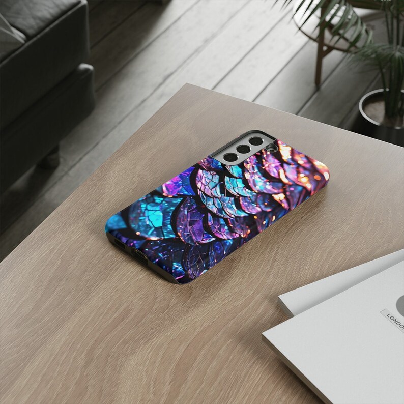 Op de afbeelding: Een telefoonhoesje met een kleurrijk, iriserend ontwerp dat lijkt op vissen schubben. De hoes is gemaakt van duurzaam materiaal en heeft een verhoogde camera-uitstulping voor bescherming.