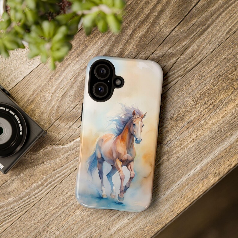May include: A phone case featuring a watercolour painting of a brown horse galloping across a field. The case has a camera cutout for a dual-lens camera.