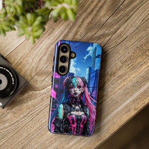 Może przedstawiać: Etui na telefon z kolorową ilustracją kobiety z r&oacute;żowymi i niebieskimi włosami. Kobieta ma na sobie czarną sk&oacute;rzaną kurtkę i r&oacute;żowo-czarny gorset. Tło to panorama miasta z niebieskim niebem.