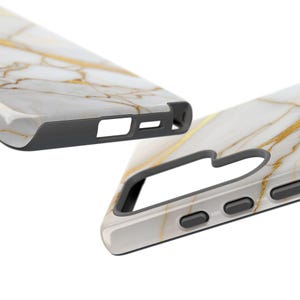 May include: A white and gold marble phone case with a black bumper. The case has cutouts for the camera and buttons.