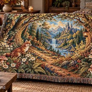 May include: A woven throw blanket featuring a detailed landscape scene with a fox sitting among white daisies and red mushrooms in a forest. The background displays a winding path, a waterfall, mountains, and a castle, all framed by trees.