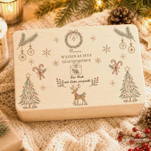 Könnte beinhalten: Eine rechteckige, helle Holzbox mit weihnachtlichen Illustrationen wie einem Kranz, Tannenbäumen, Zuckerstangen, Schneeflocken und einem Rentier. Der Text lautet Meine WEIHNACHTS GESCHENKEBOX und Für Dich mit Liebe verpackt.