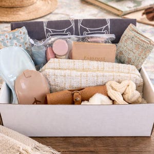 A thoughtful travel gift box filled with practical and stylish essentials for any trip. 
What's Included

✔ Silk eye mask 
✔ Sunglasses holder 
✔ 2 pairs cozy socks 
✔ Passport cover & luggage tag
✔ Set of 3 scrunchies 
✔ TSA travel bottle set 
✔ Travel pouch 
✔ Drawstring shoe bag