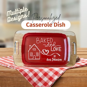 May include: A personalized casserole dish with a red interior and clear glass lid. The dish features the words "Baked with Love" and a house graphic. The text "Multiple Designs!" is above the dish.