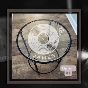 May include: A black metal side table with a glass top. The glass top has a white vinyl record and turntable design etched into it. The name "JAMES" is also etched into the glass.