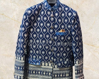 Puede incluir: Una chaqueta de terciopelo azul con un patrón floral plateado y un pañuelo de bolsillo dorado. La chaqueta tiene un cuello mandarín y un cierre de botón.