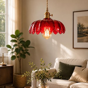 May include: A pendant light featuring a scalloped, deep red glass shade with a petal-like design. The fixture includes a brass-toned metal socket and a twisted fabric cord. An exposed filament light bulb hangs centred within the glass shade.