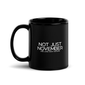 Könnte beinhalten: Schwarze Keramik-Kaffeetasse mit weißem Text, der "Not Just November, One Land Many Nations" lautet.