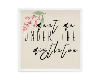 Puede incluir: Cojín cuadrado con el texto "meet me UNDER THE mistletoe" en escritura negra. El cojín tiene un fondo beige con una ilustración de acuarela de bayas rojas y hojas verdes en la esquina superior izquierda.