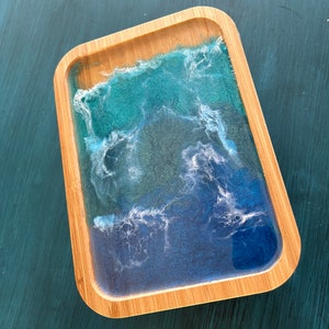 May include: A rectangular wooden tray with a blue and green resin inlay that resembles ocean waves. The resin is clear and has white swirls throughout.