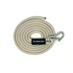 May include: A coiled beige rope with a braided texture, featuring a silver-colored metal snap hook at one end. A rectangular black fabric tag is attached to the rope, displaying the white printed text "Your Name Here" in a clear font.