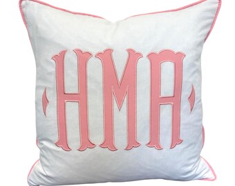 May include: White square pillow with pink embroidered initials HMA. The pillow has a pink trim around the edges. The letters are in a decorative font.