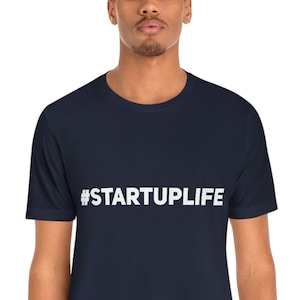 Könnte beinhalten: Ein marineblaues T-Shirt mit weißem Text, der "#STARTUPLIFE" lautet