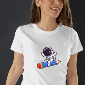Astronauta volando en un lápiz, regalo para escritor, lindo gráfico de dibujos animados, regalo para profesor, autor, creativo presente camiseta unisex
