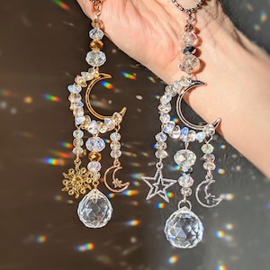 May include: Two crystal suncatchers with crescent moon charms, one with gold accents and one with silver accents. Both feature crystal beads, a crystal ball, and a star charm.