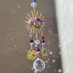 May include: A gold eye-shaped suncatcher with purple and clear crystal beads, a crystal prism, and gold sun and moon charms.