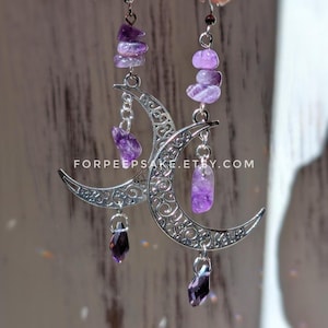 May include: Dangle earrings featuring silver-toned crescent moon charms with intricate filigree patterns. Each earring includes stacked purple amethyst chip beads and a faceted dark purple crystal drop. The text FORPEEPSAKE.ETSY.COM is visible.