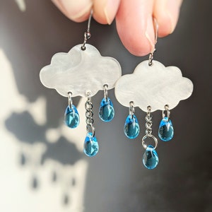 May include: White cloud shaped earrings with blue raindrop charms hanging from the bottom.
